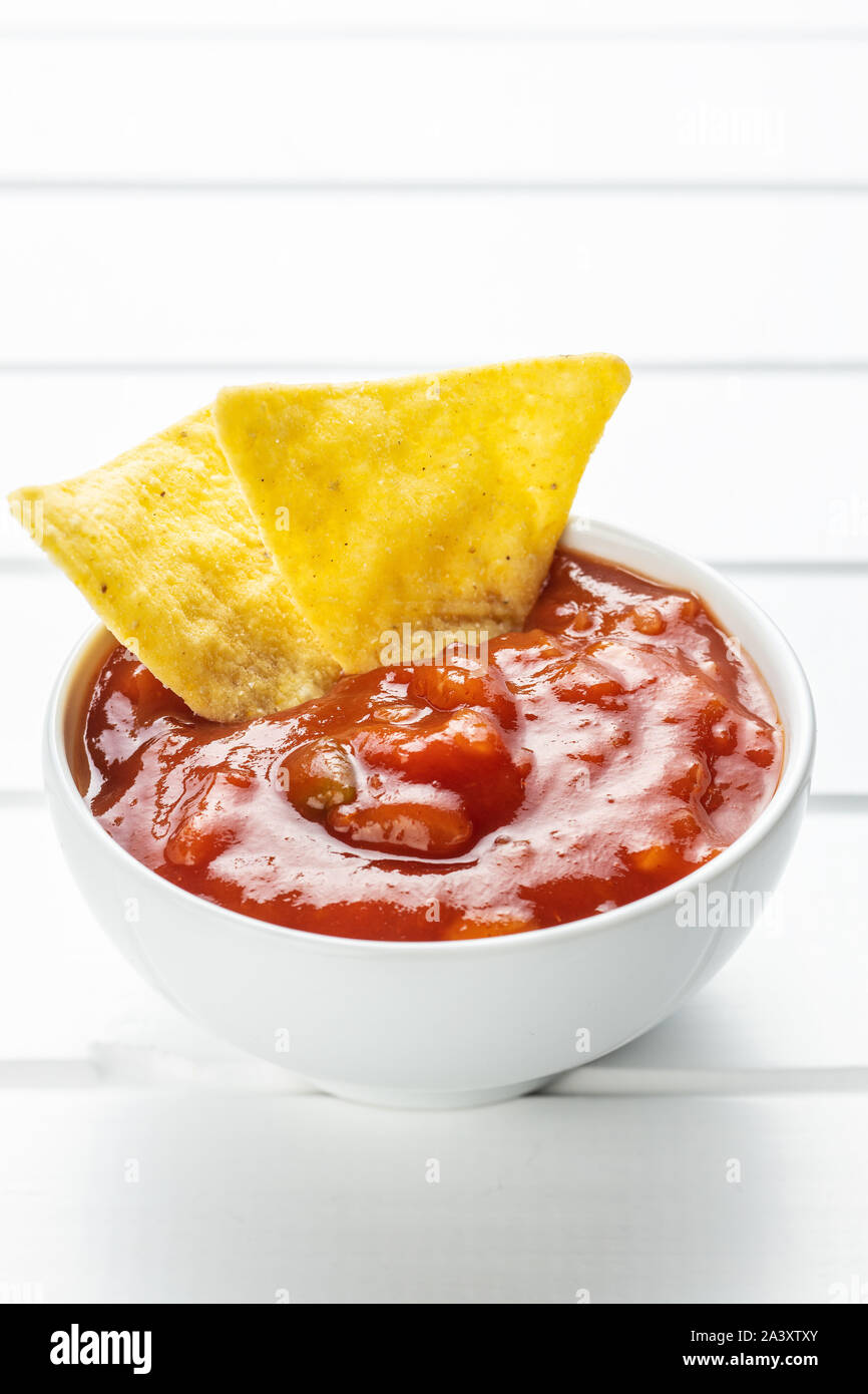 Corn nacho chips and tomato dip. Yellow tortilla chips and salsa on white table. Stock Photo