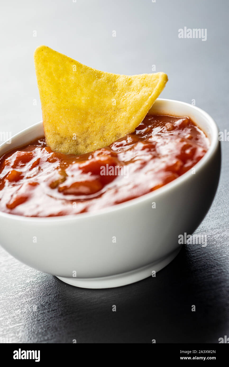 Corn nacho chips and tomato dip. Yellow tortilla chips and salsa on black table. Stock Photo