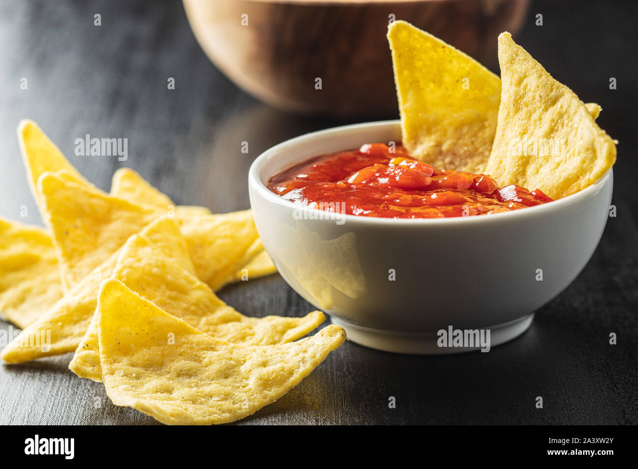 Corn nacho chips and tomato dip. Yellow tortilla chips and salsa on black table. Stock Photo