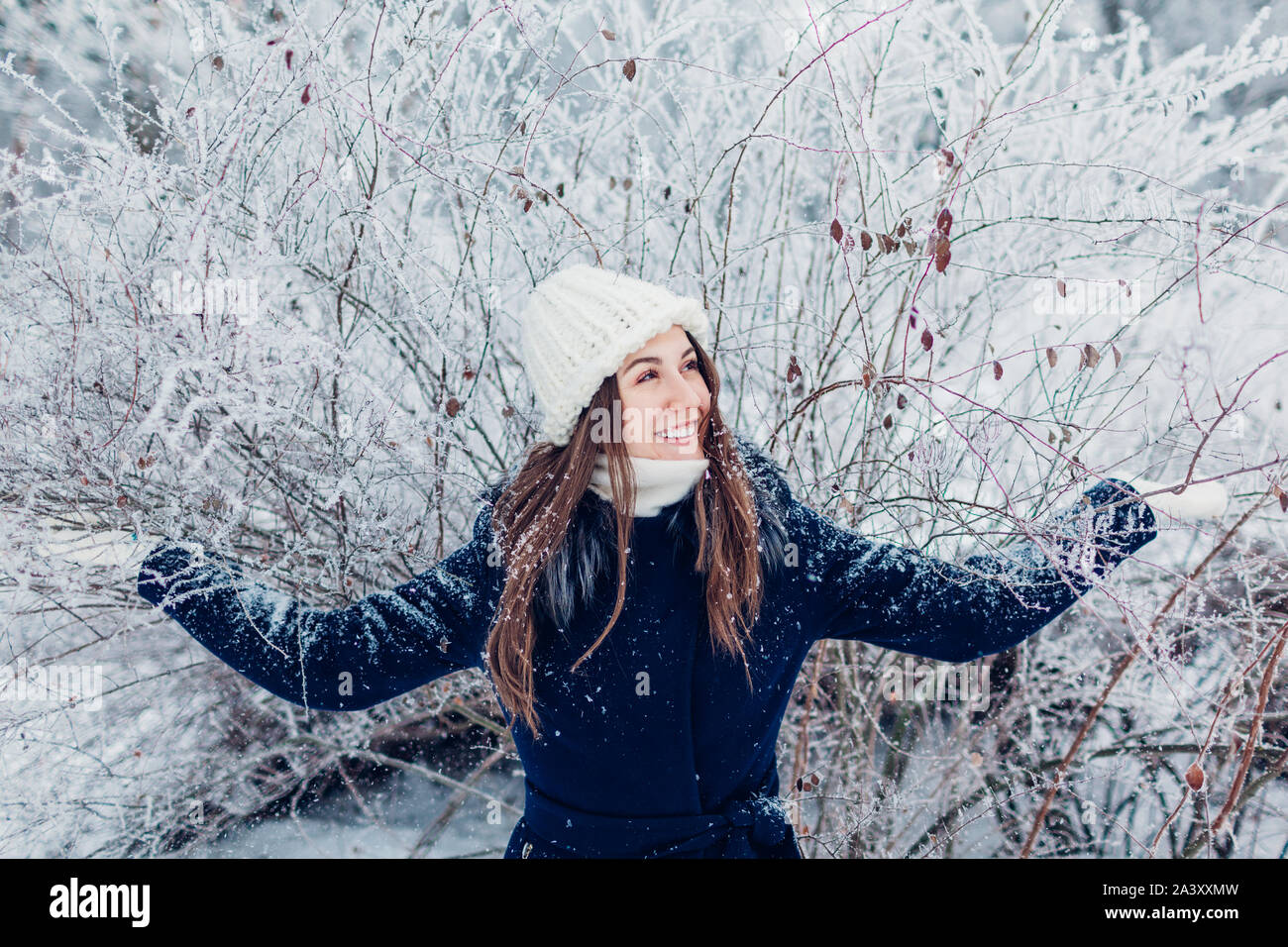 Winter activities. Young woman shaking branches with hoarfrost and snow ...