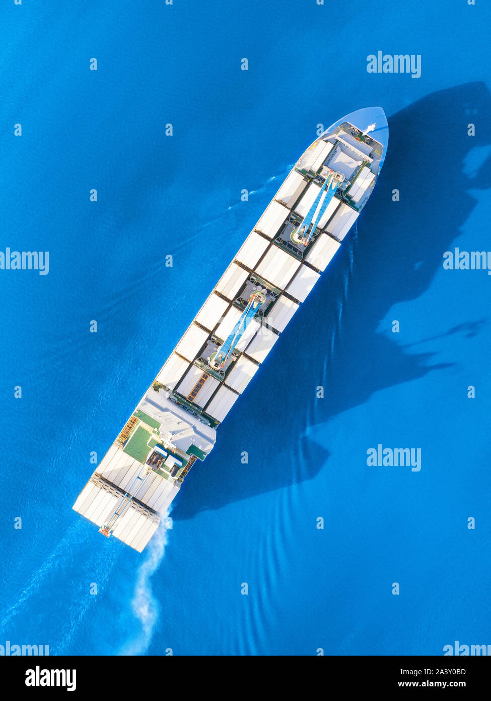 Large full loaded container ship with cranes sailing bright blue sea. Top aerial view Stock Photo