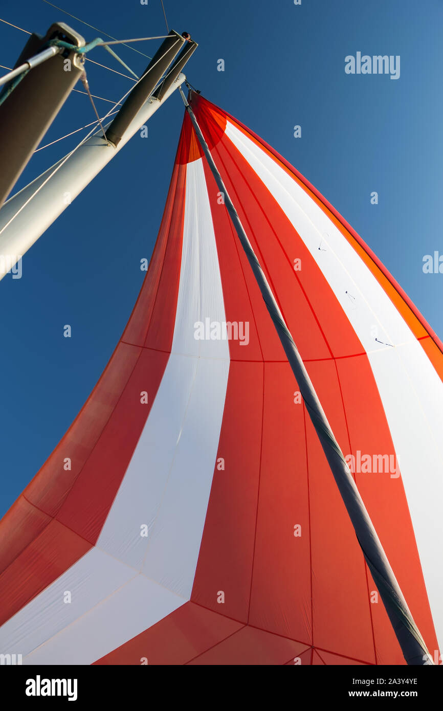White-red developing sail on a yacht mast against the blue sky, bottom view. Traveling by sea on sunny day. Leisure activities at sea. Competitions on Stock Photo