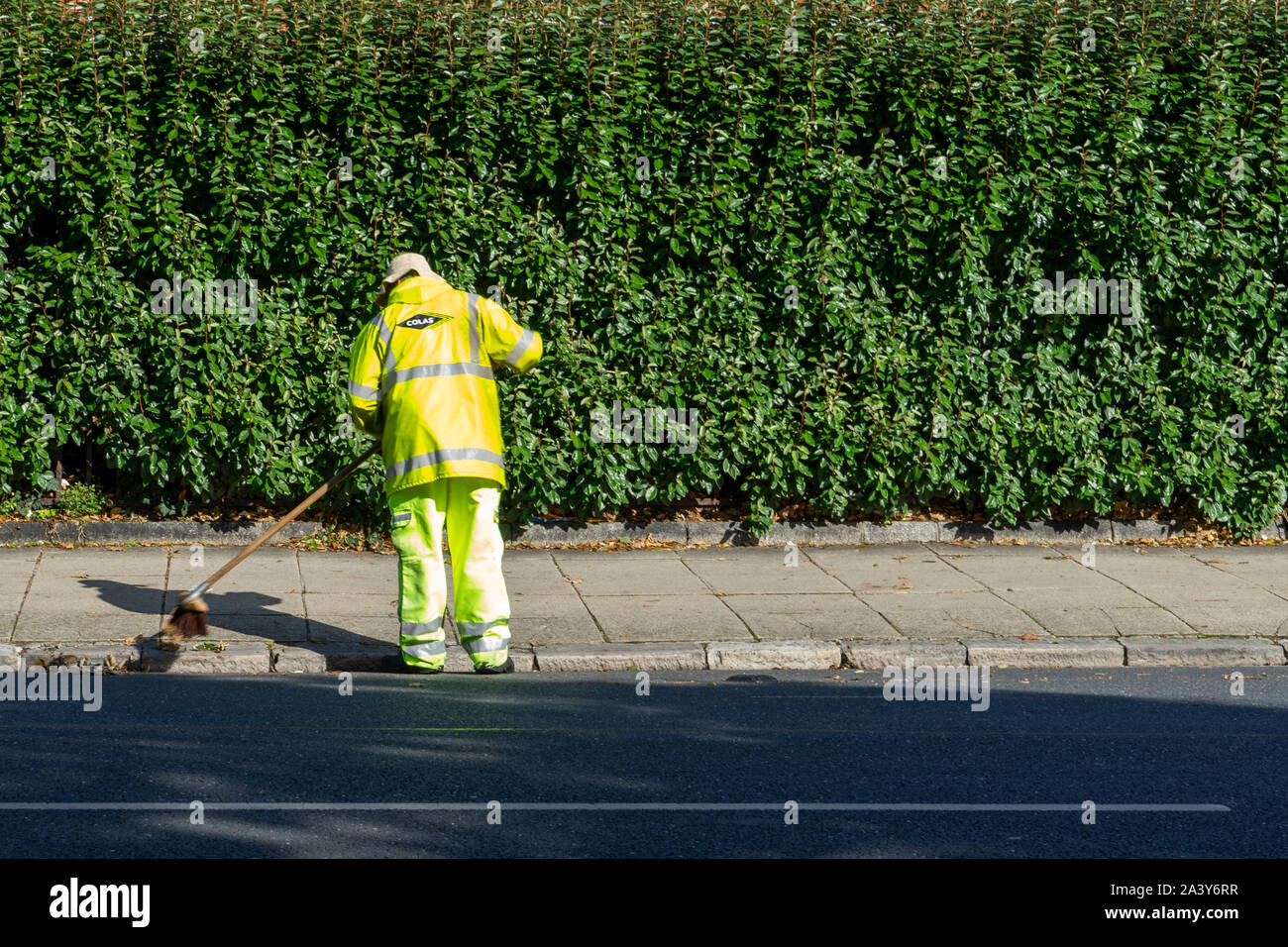 A road sweeper in high visibility clothing sweeping the roadside with a broom Stock Photo