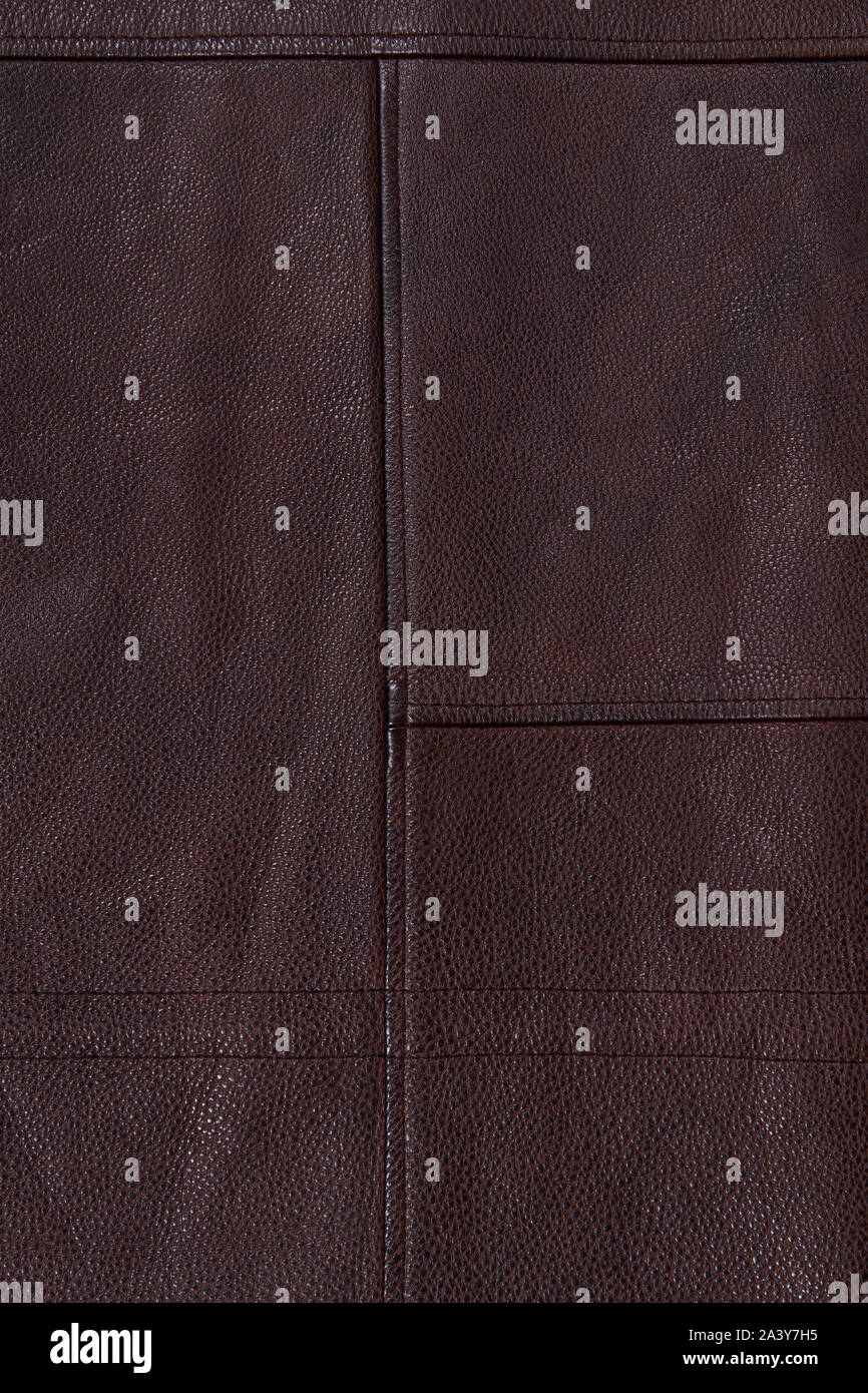 Dark brown stitched leather background. Asymmetric seams. Rough surface with free space. Expensive material sample. Handwork. Seat upholstery. Stock Photo