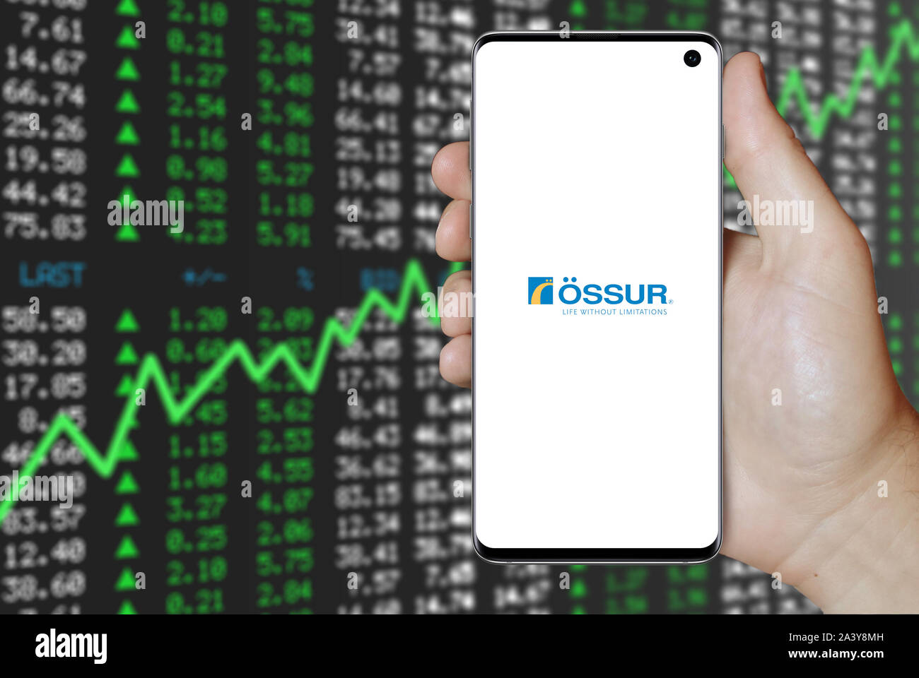 A man holds a phone displaying the logo of company Össur listed on OMX Copenhagen. Positive stock market. Credit: PIXDUCE Stock Photo