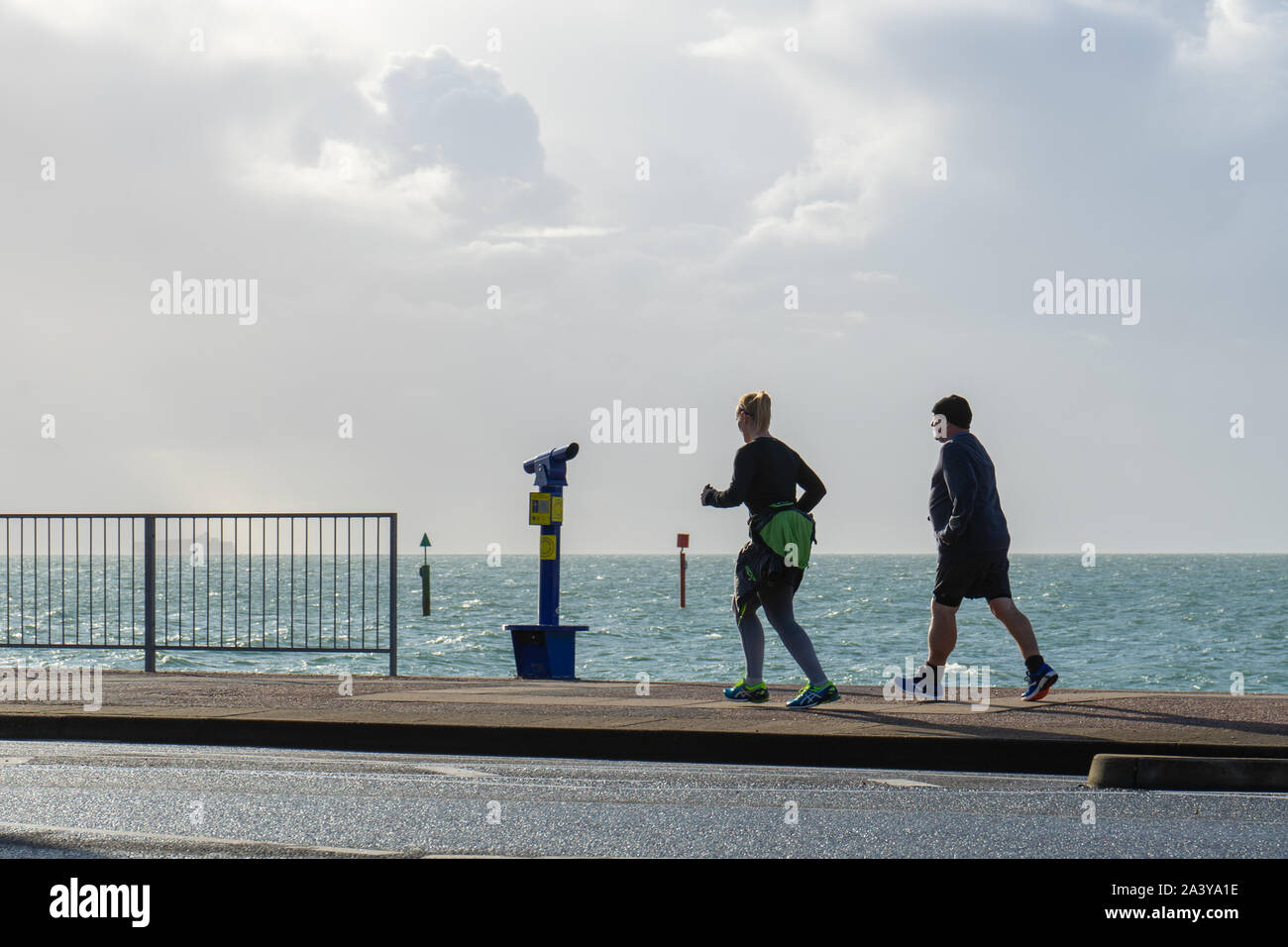 middle aged male and female runners jogging along the promenade at the seaside Stock Photo