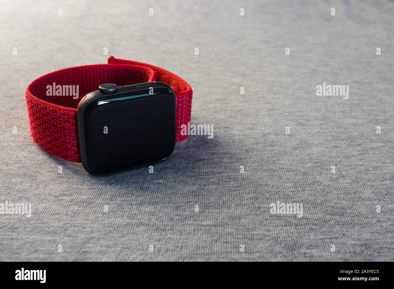 Black smartwatch with a red band, lying on a soft, grey fabric cloth