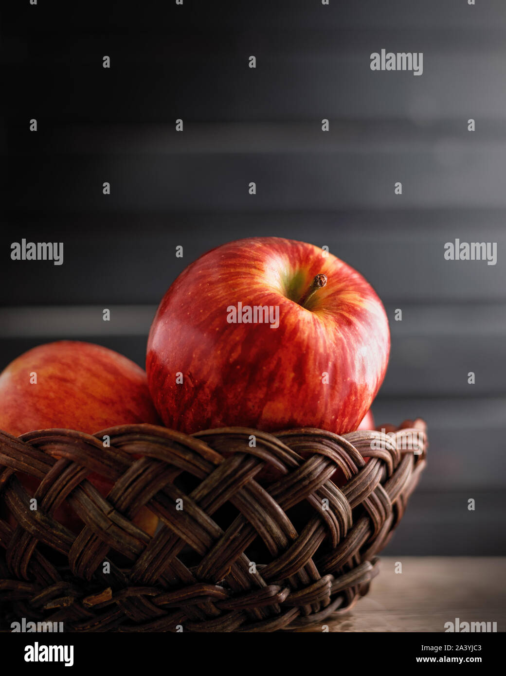 Beautiful and fresh red apples in a vine basket closeup, dark black moody background Stock Photo