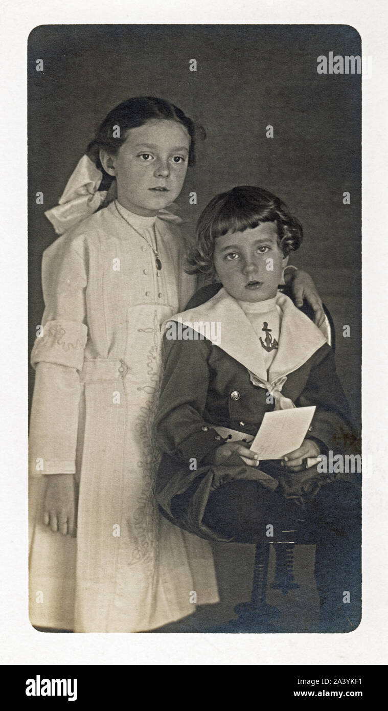 A boy and a girl, siblings, circa 1910 posing in dress up clothing. Little boy is wearing a sailor suit and older sister in a white lacey dress. Stock Photo