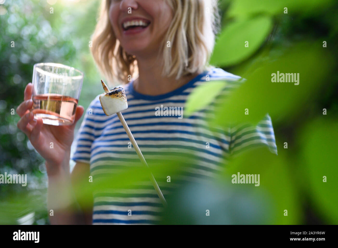 Smiling woman holding glass of wine and toasted marshmallow Stock Photo