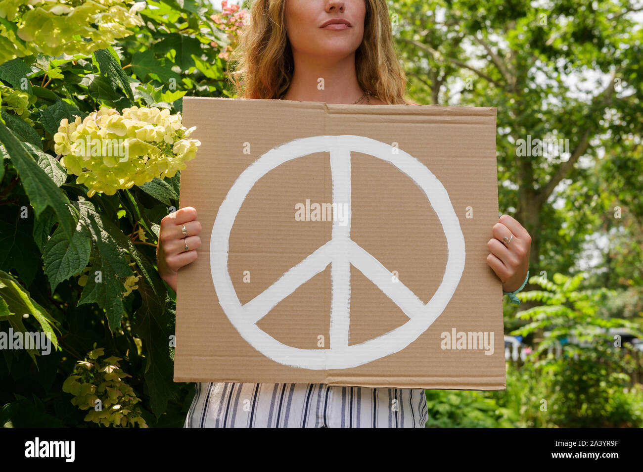 Woman holding peace symbol by trees Stock Photo