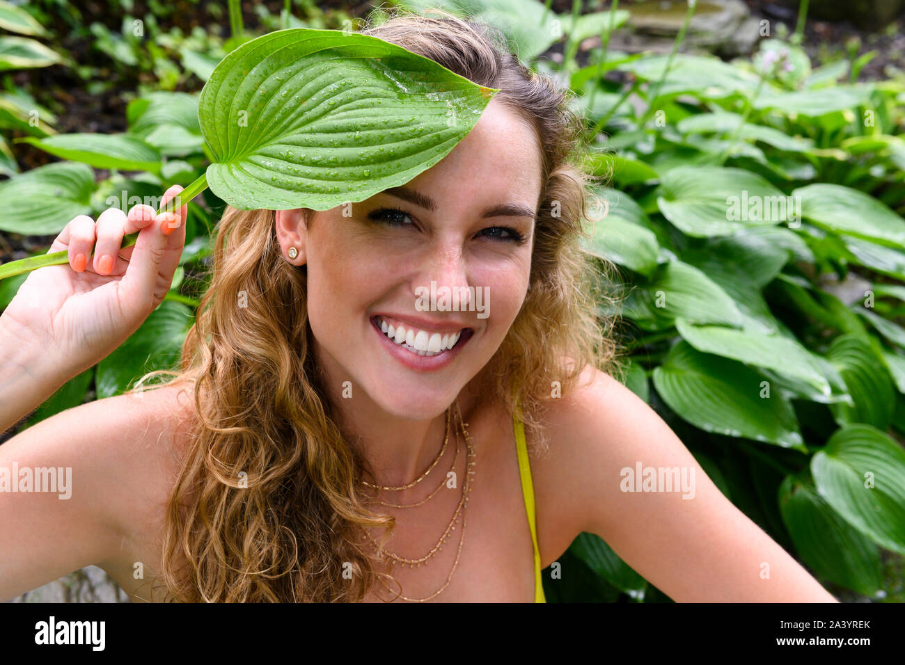 Smiling young woman holding green leaf Stock Photo