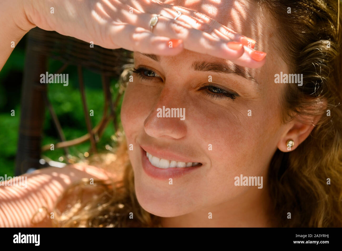 Smiling young woman shielding her eyes Stock Photo