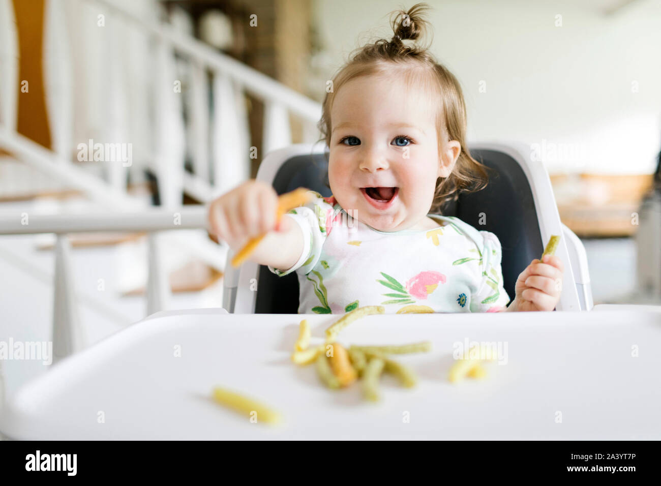 Baby girl eating in high chair Stock Photo