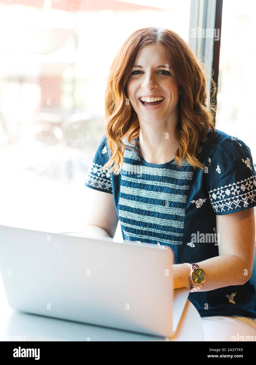 Smiling woman using laptop in cafe Stock Photo