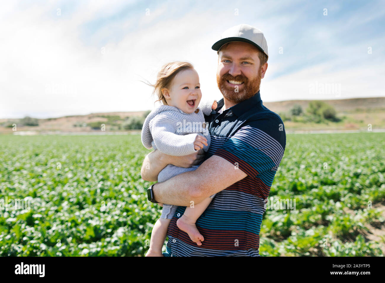 Smiling father holding baby girl in crop field Stock Photo