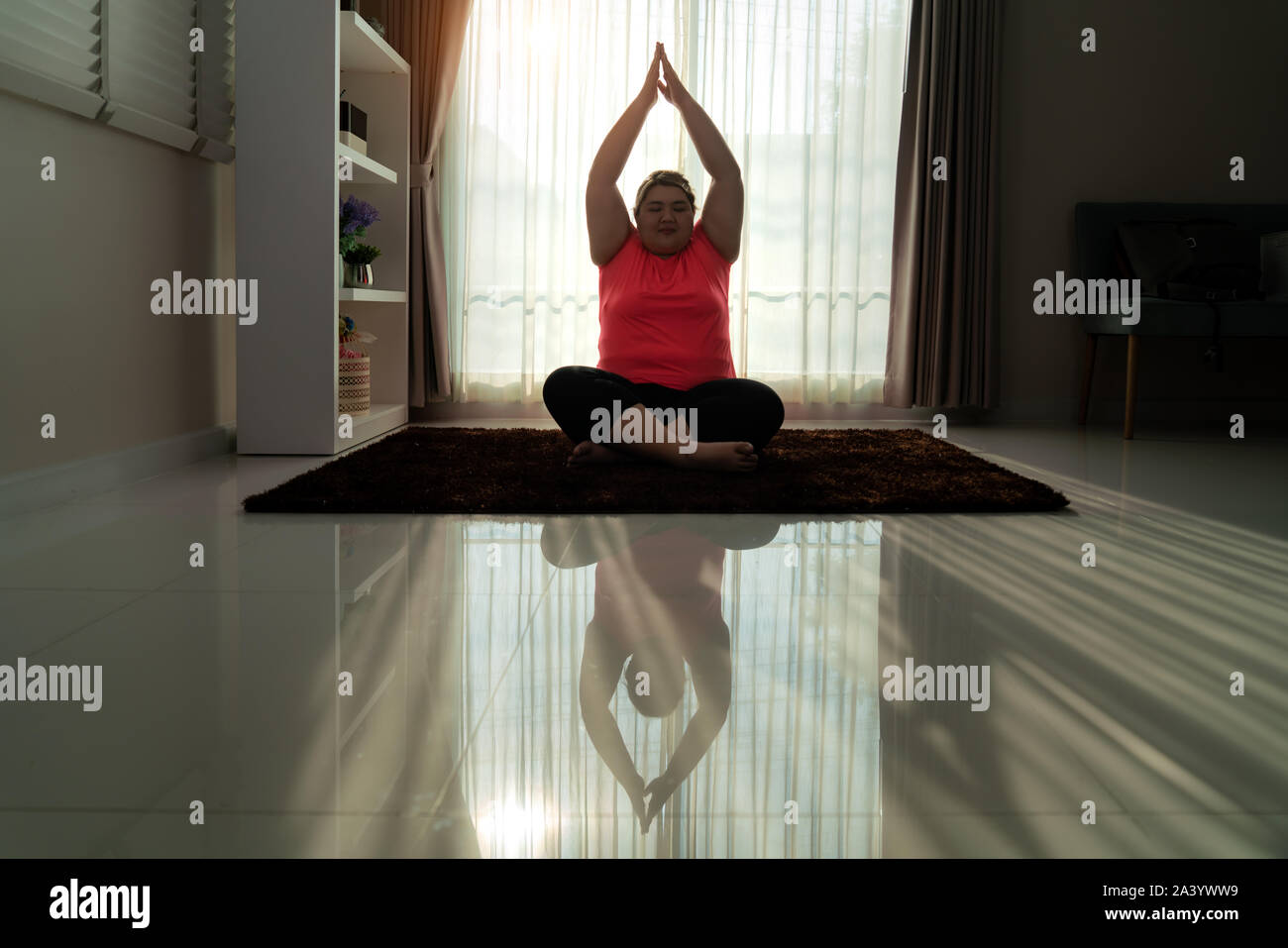 Asian Overweight woman exercising yoga Easy Pose alone on the floor in house, yoga meditation exercise at home. Fat women take care of health and want Stock Photo