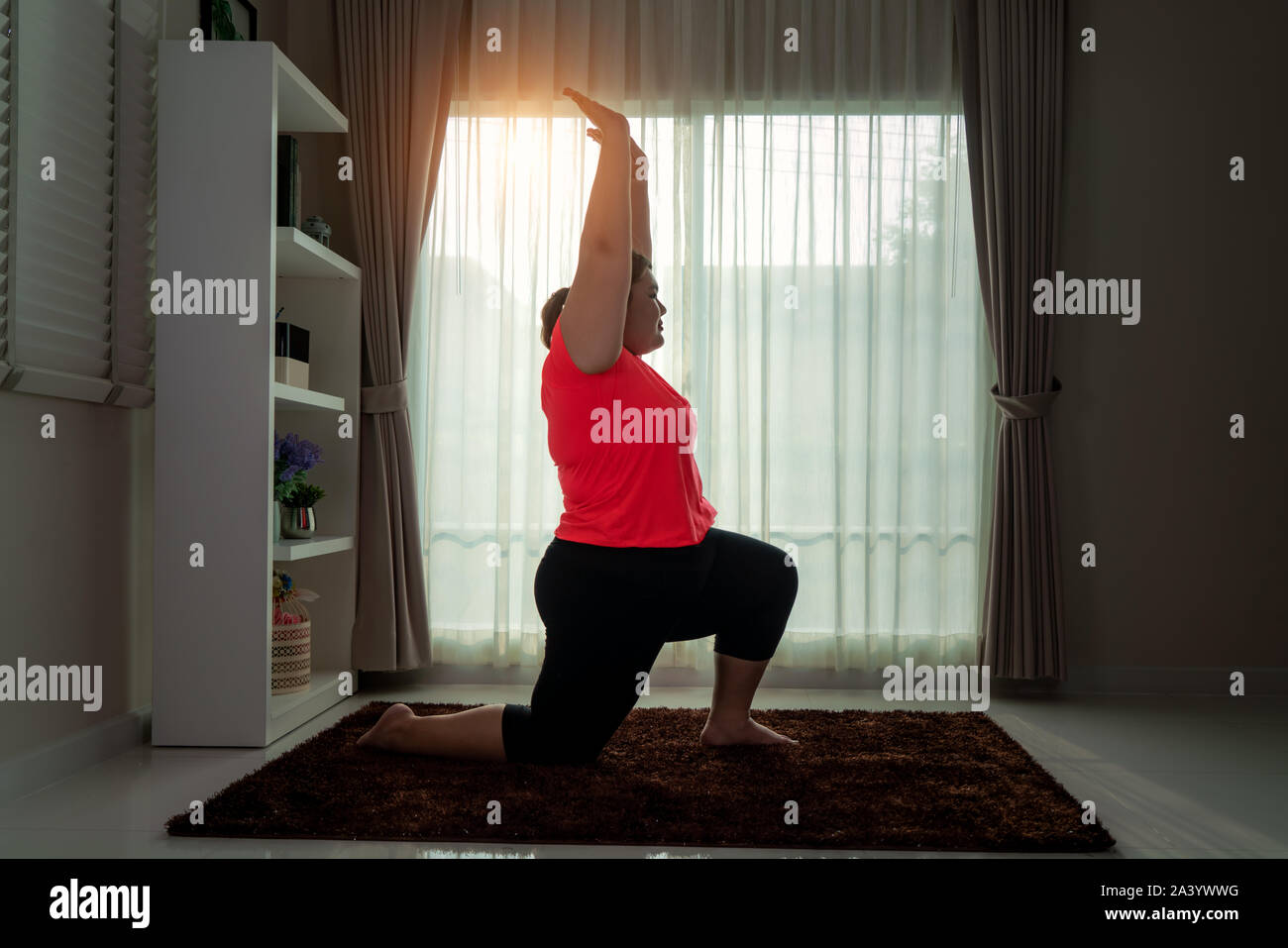 Asian Overweight woman exercising yoga High Lung pose alone on the floor in house, yoga meditation exercise at home. Fat women take care of health and Stock Photo