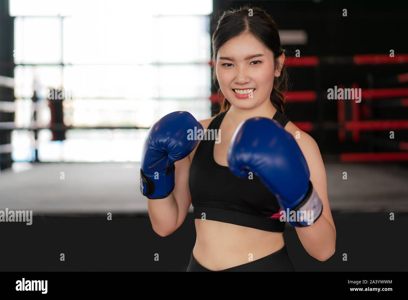 Boxer woman. Young Asian Boxing fitness woman smiling happy wearing blue boxing gloves with Boxing Stadium in background. Portrait of sporty fit for h Stock Photo
