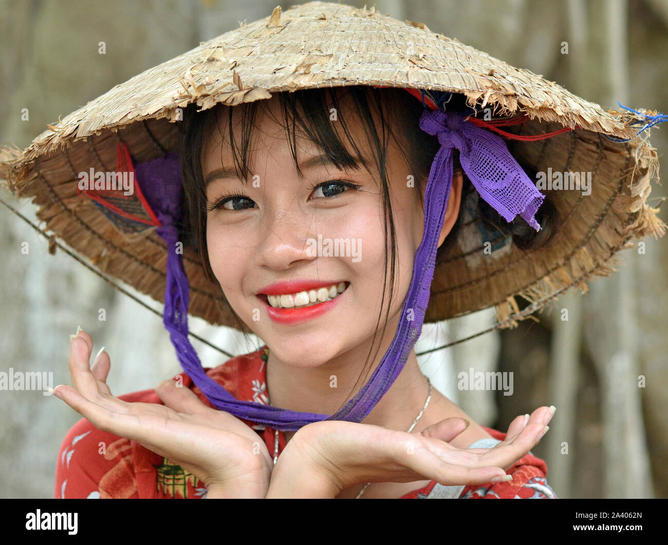 Young Vietnamese woman wears an old Asian conical hat (rice hat) and poses for the camera. Stock Photo