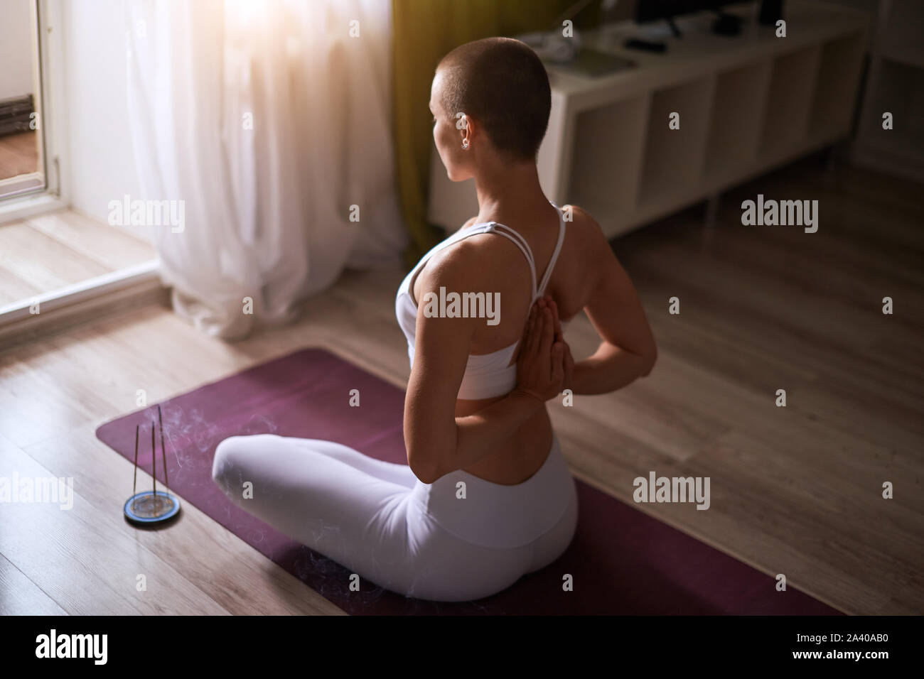 Caucasian short-haired woman practicing yoga with namaste behind the back, sitting in seiza exercise, vajrasana pose. Wearing in white leggins and whi Stock Photo