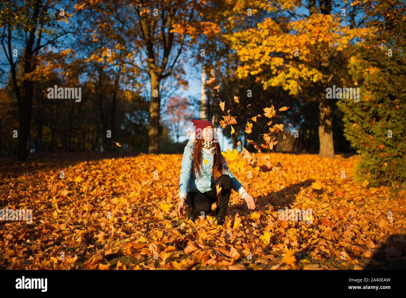 Happiness carefree leisure concept. Redhaired long hair woman relaxing in autumn park throwing leaves up in the air. Beautiful girl in orange forest f Stock Photo