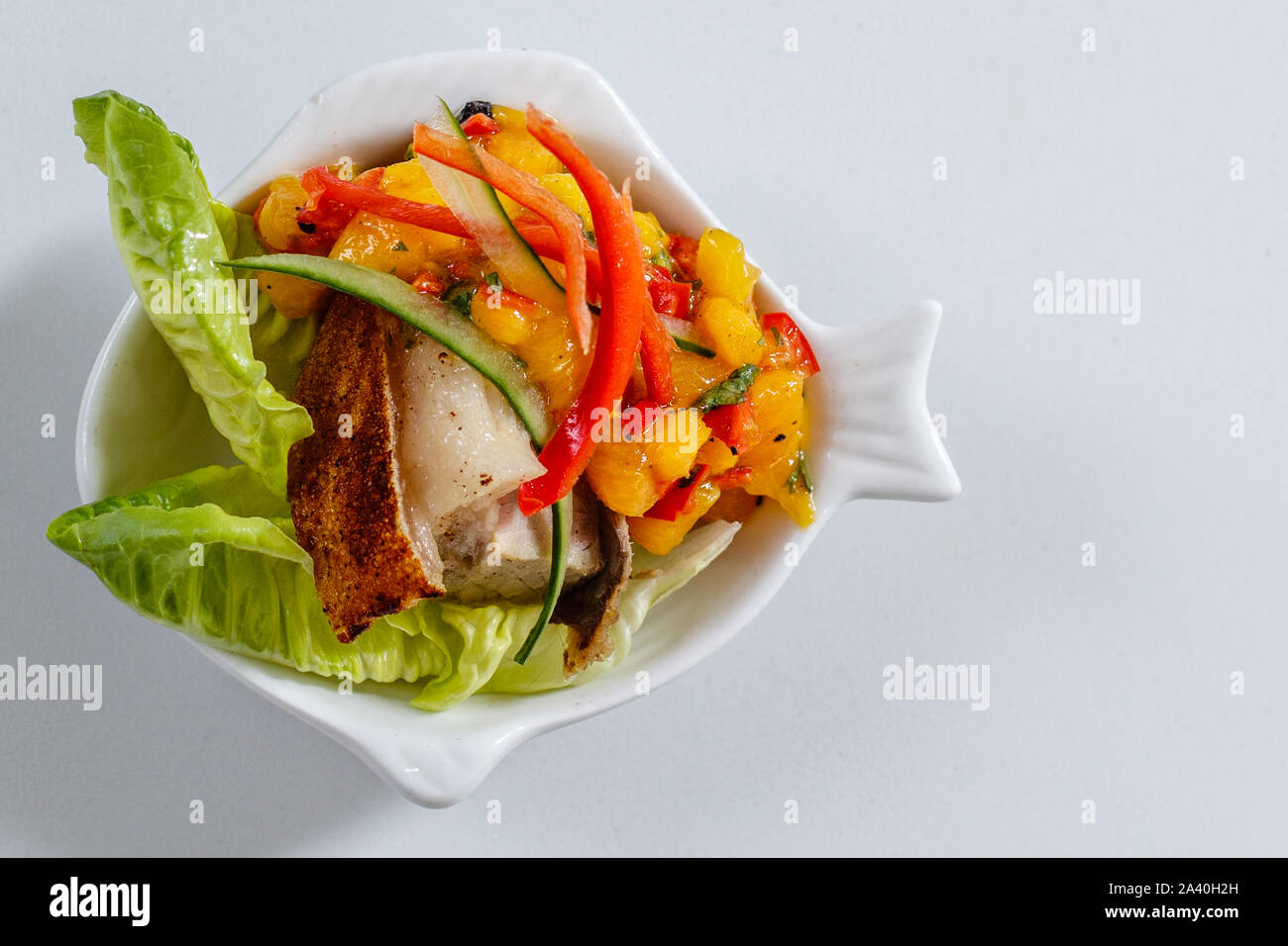 Jamaican Pork Belly appetizer with Mango & Lime Salsa served on young lettuce in white ceramic