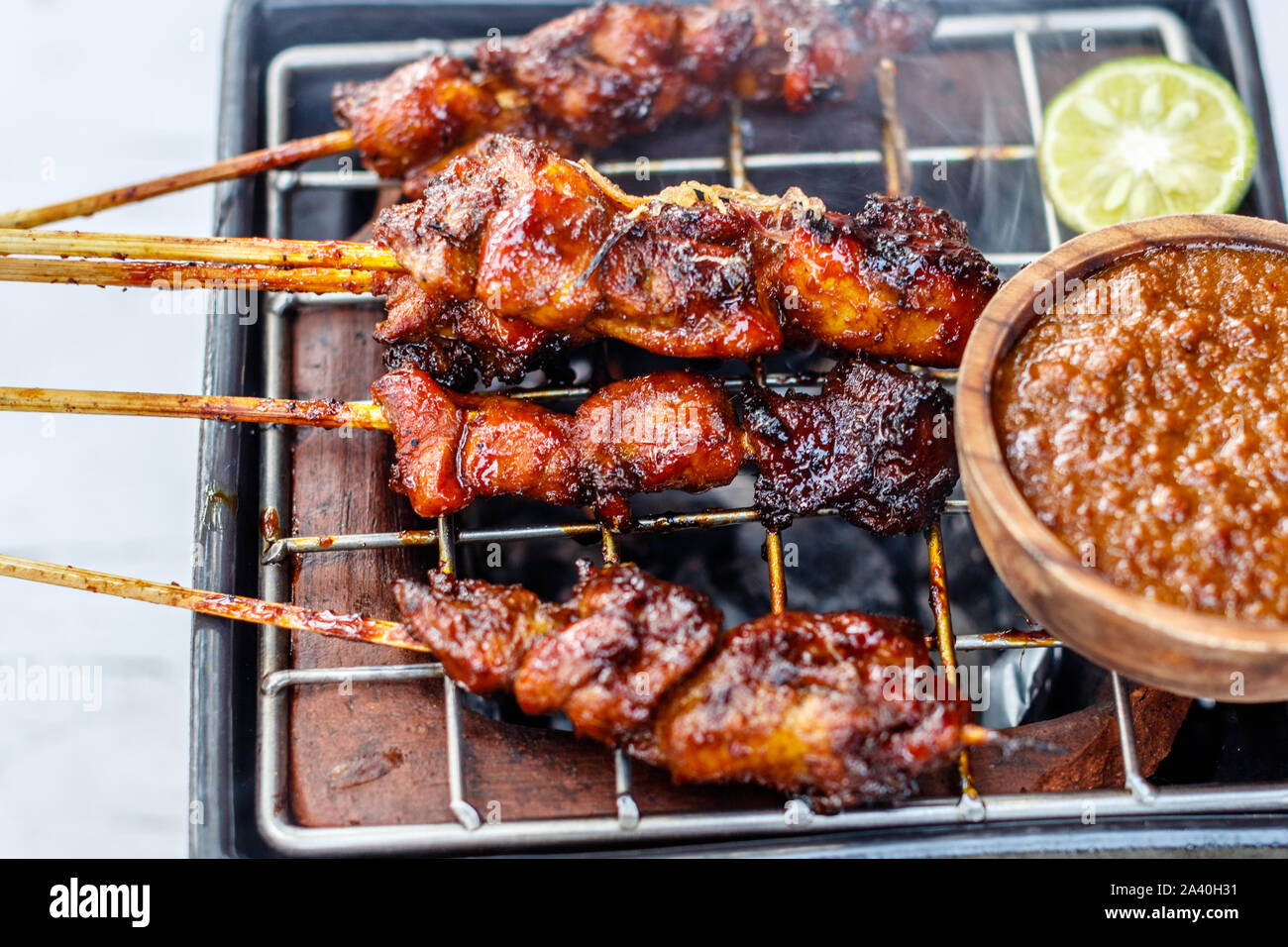 Sate ayam - grilled chicken meat on wooden skewers with sambal kacang - peanut dipping sauce. Served on a ceramic charcoal grill. Stock Photo