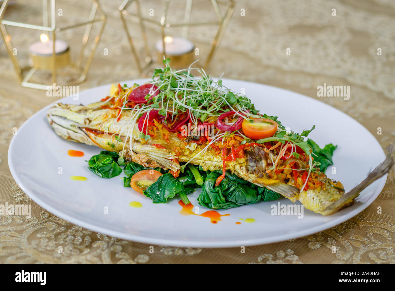 Whole Baby Barramundi with Kai-lan (Chinese broccoli), Chilli, Ginger, Turmeric, Coriander and Lemon. Decorated with onion colored with beetroot juice. Stock Photo