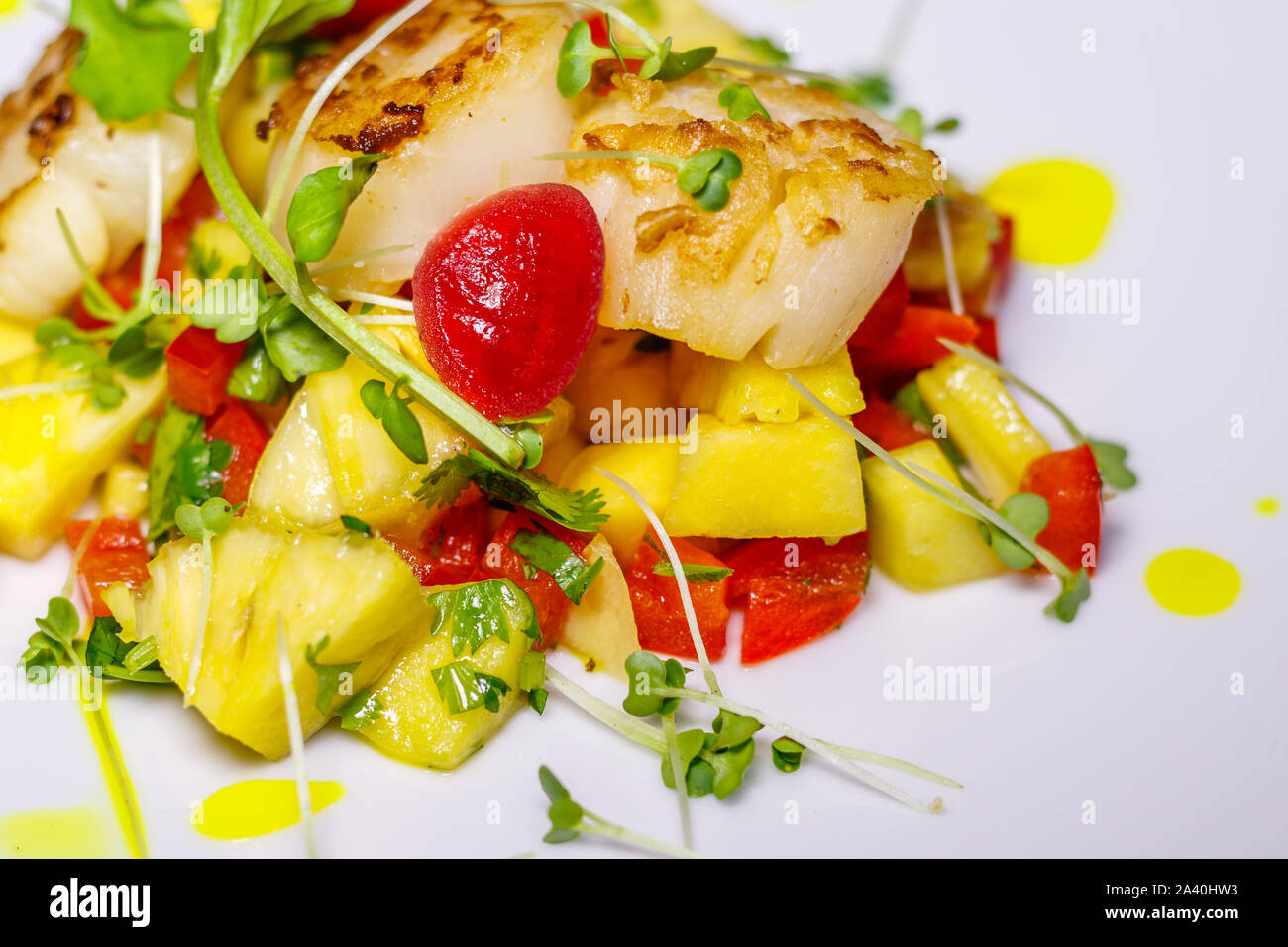 White ceramic plate with grilled King scallop with pineapple, onion colored with beetroot sauce, red bell pepper, decorated with bean sprouts. Side vi Stock Photo