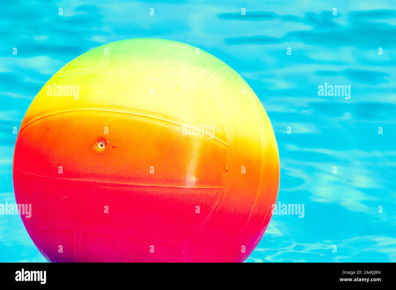 Bright rainbow ball in a swimming pool turquoise water. Concept of a joyful summer vacation. Idea of outdoor games in the summertime. Stock Photo