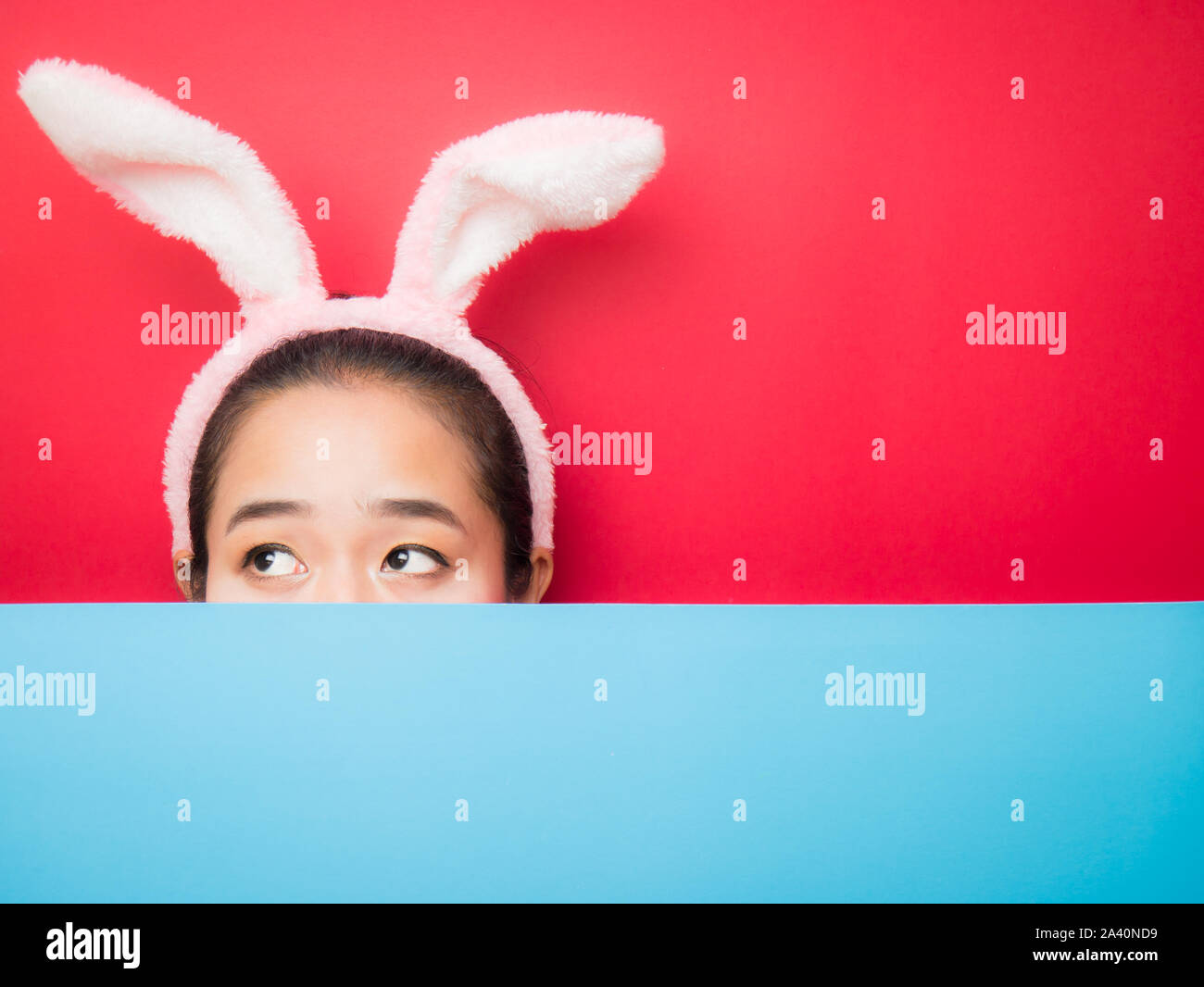 Cute teenage girl wearing bunny ears headband on sky and red background. Attractive young woman on a bright red and sky background. Stock Photo