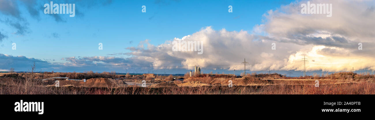 Panoramic view of an industrial district in Germany. Electricity towers, funnels and wind mills. Windpark far away on the horizont. Dramatical wide sk Stock Photo