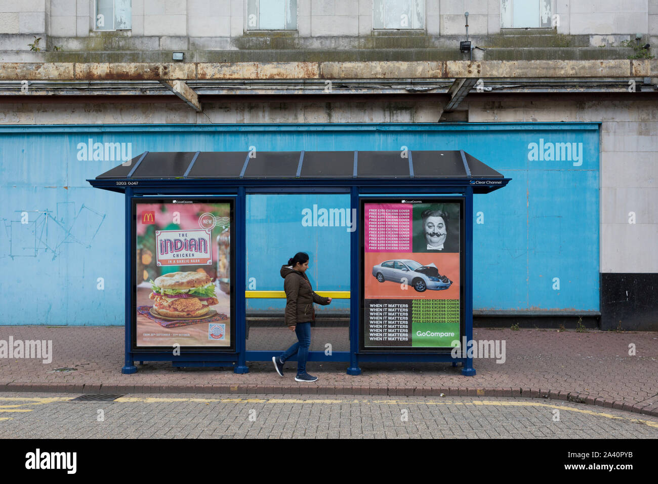 A passer-by walks past a bus shelter featuring Indian food and Go Compare insurance plus a blue hoarding outside a closed entertainment venue in Dartford, on 3rd October 2019, in Dartford, Kent, England. Voters in Dartford voted 64% in favour of Brexit during the 2016 referendum. Stock Photo