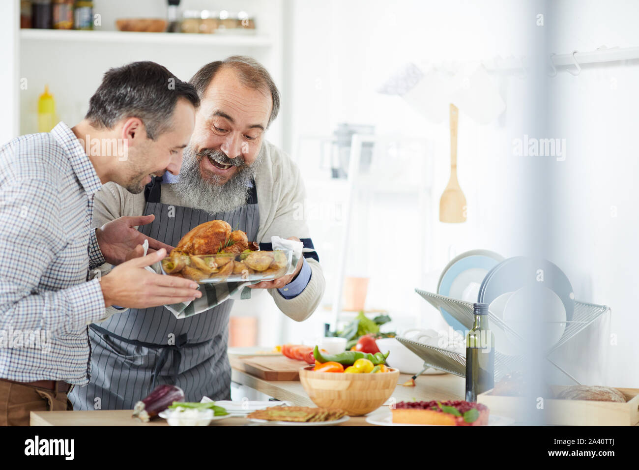 Senior man with beard and young man holding dish of roast turkey prepared for dinner at home Stock Photo