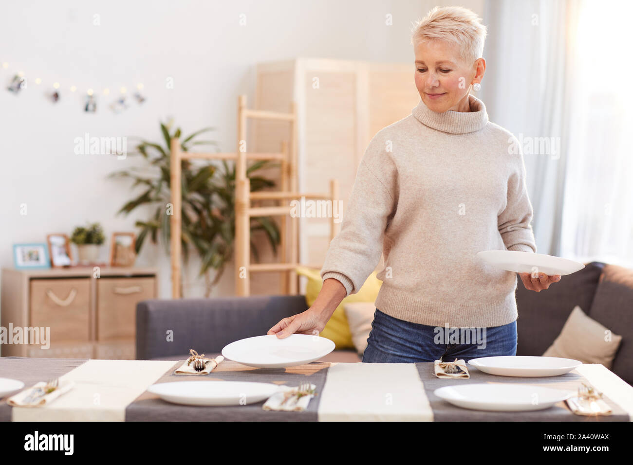 Mature woman with short blond hair putting plate on the table and serving the table before the family dinner at home Stock Photo