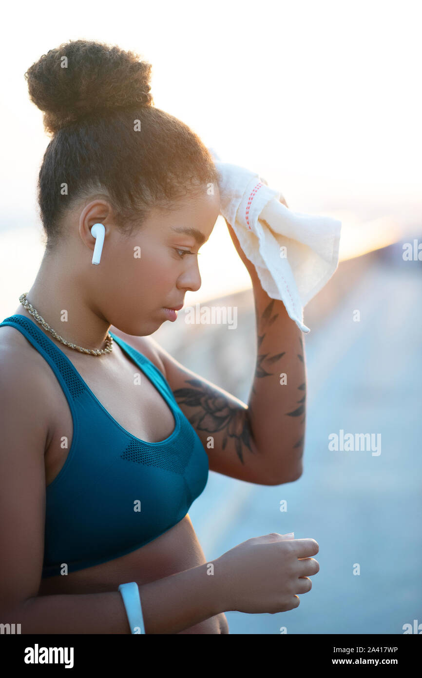 Dark-haired woman with tattoo on arm drying sweat on forehead Stock Photo