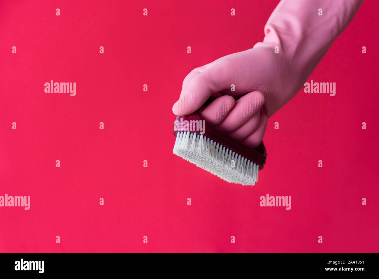 Hand in pink latex protective glove with dust brush on pink background. Cleaning and housework work concept Stock Photo