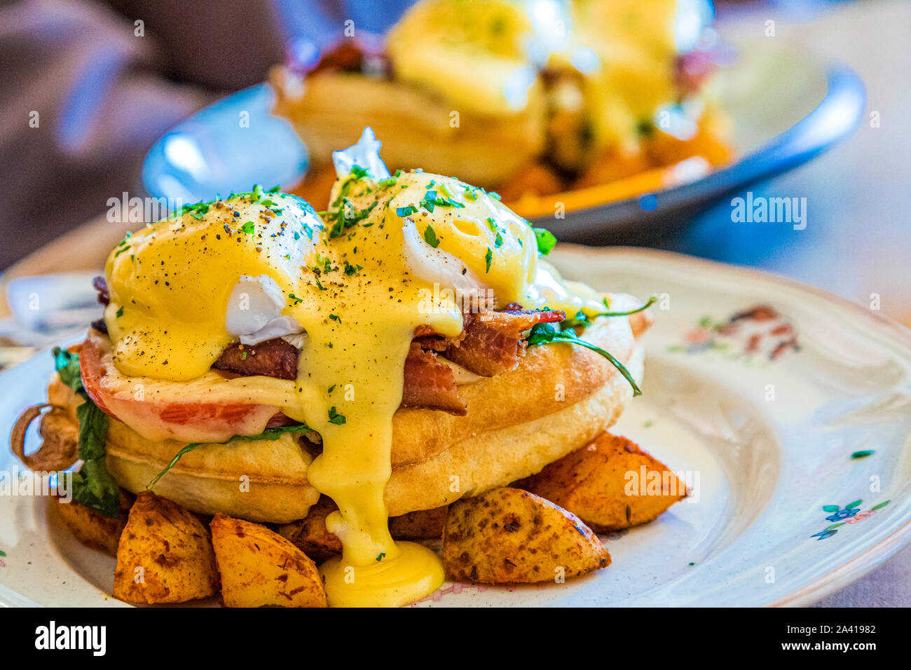 Ham and Bacon Benedict Served over Waffle and Potatoes Stock Photo