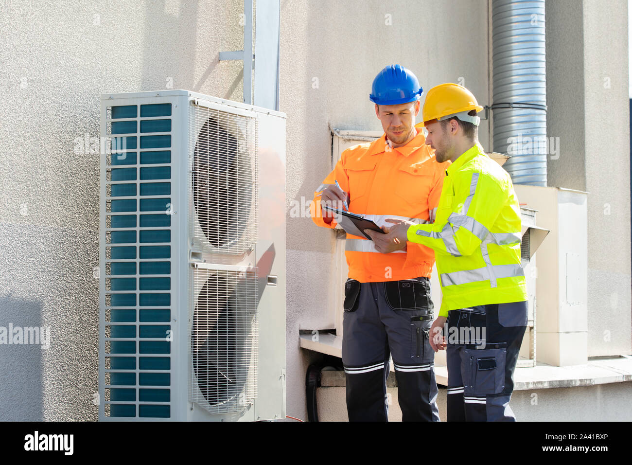 Two Electricians Men Wearing Safety Jackets Checking Air Conditioning Unit On Building Rooftop Stock Photo