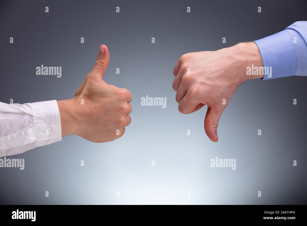 Close-up Of Two Businessman's Hands Showing Thumbs Up And Down Sign Against Gray Background Stock Photo