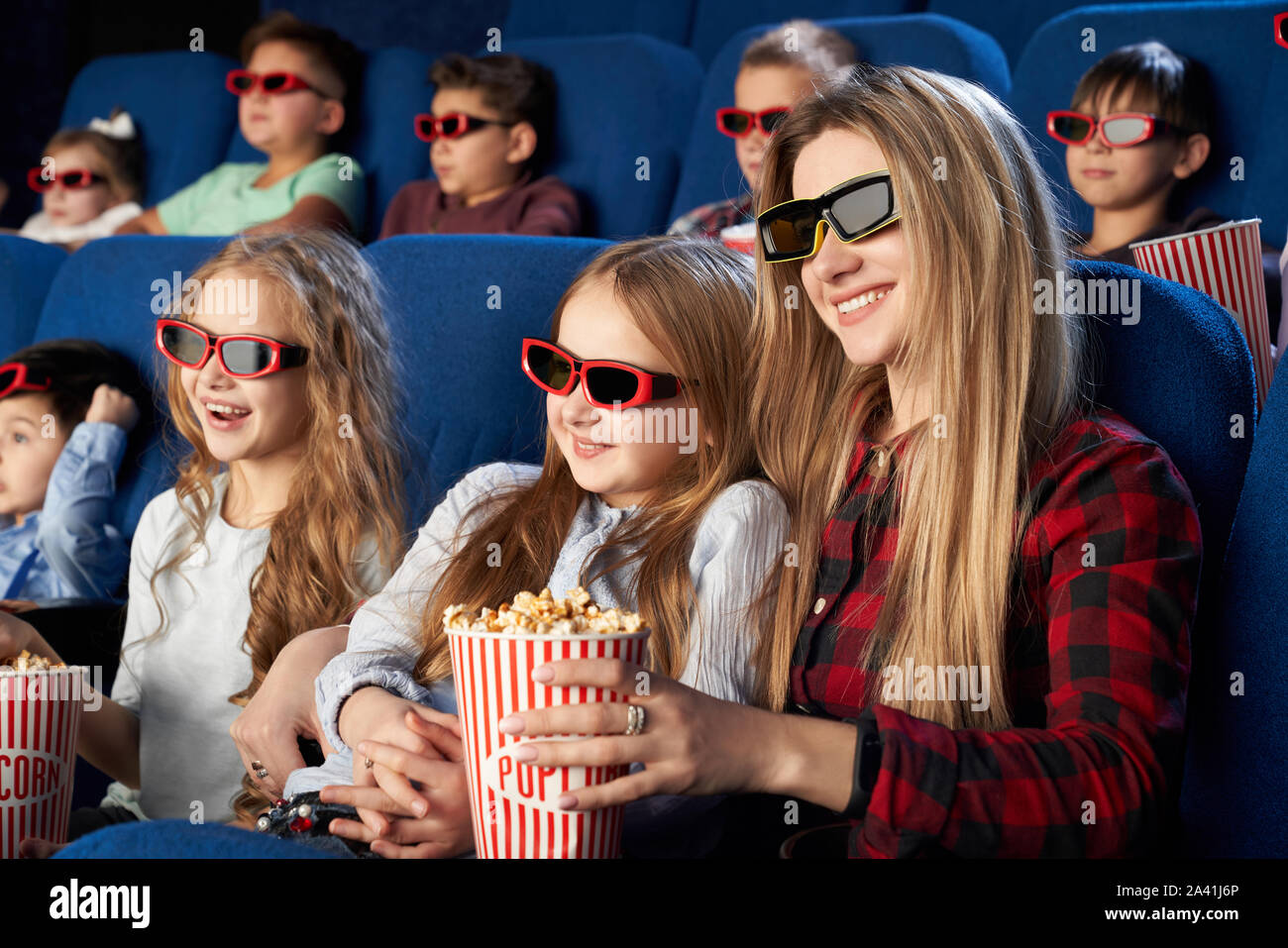Happy mother and daughter wearing 3d glasses and eating tasty popcorn in cinema. Cheerful family watching funny film and enjoying spare time together in movie house. Concept of enjoyment and fun. Stock Photo