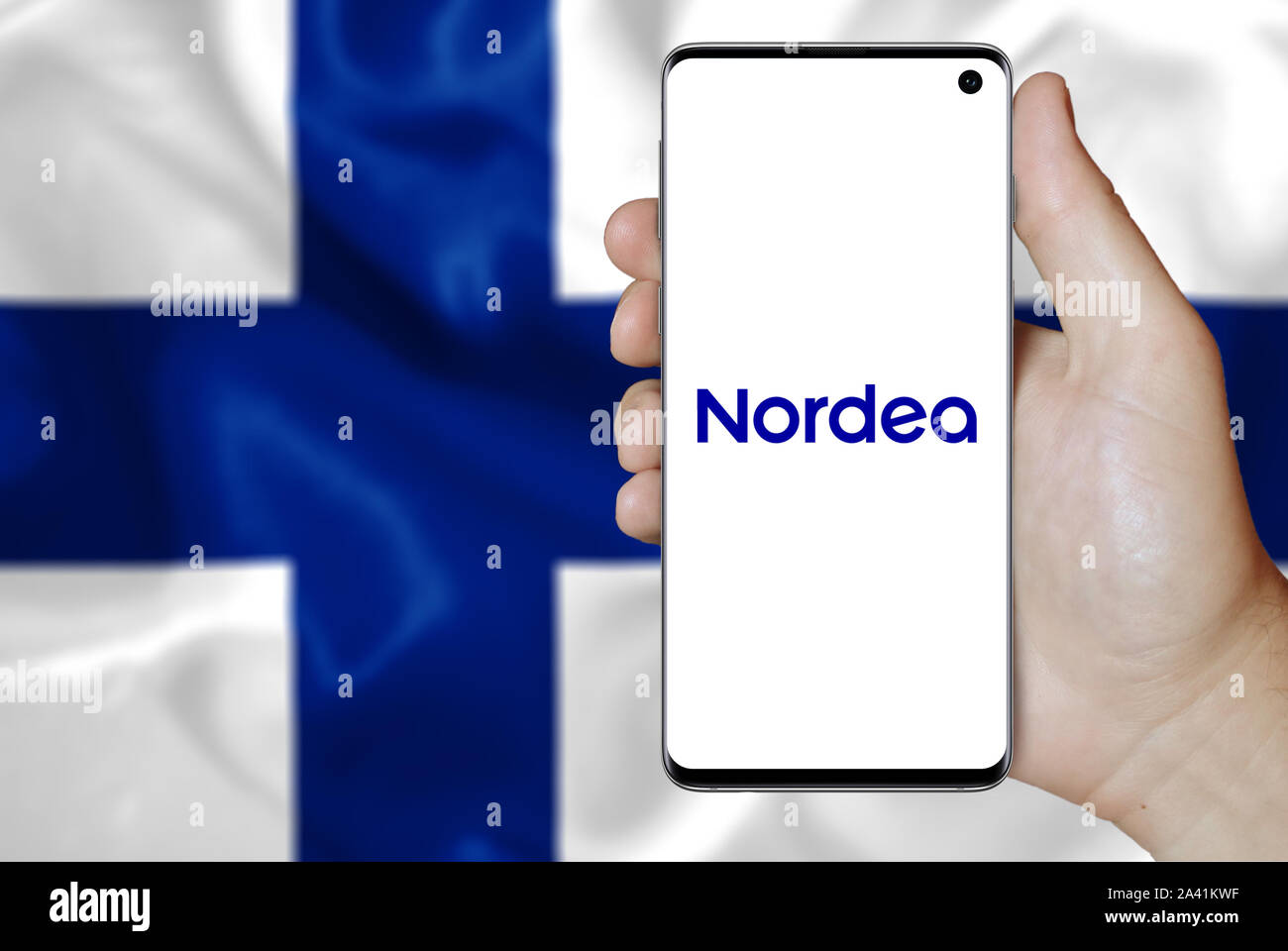 A man holds a phone displaying the logo of company Nordea Bank Abp listed on OMX Helsinki. Finish flag background. Credit: PIXDUCE Stock Photo