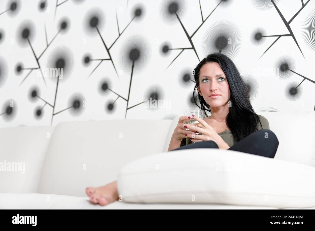 Attractive young woman relaxing on her sofa at home with a glass of ...