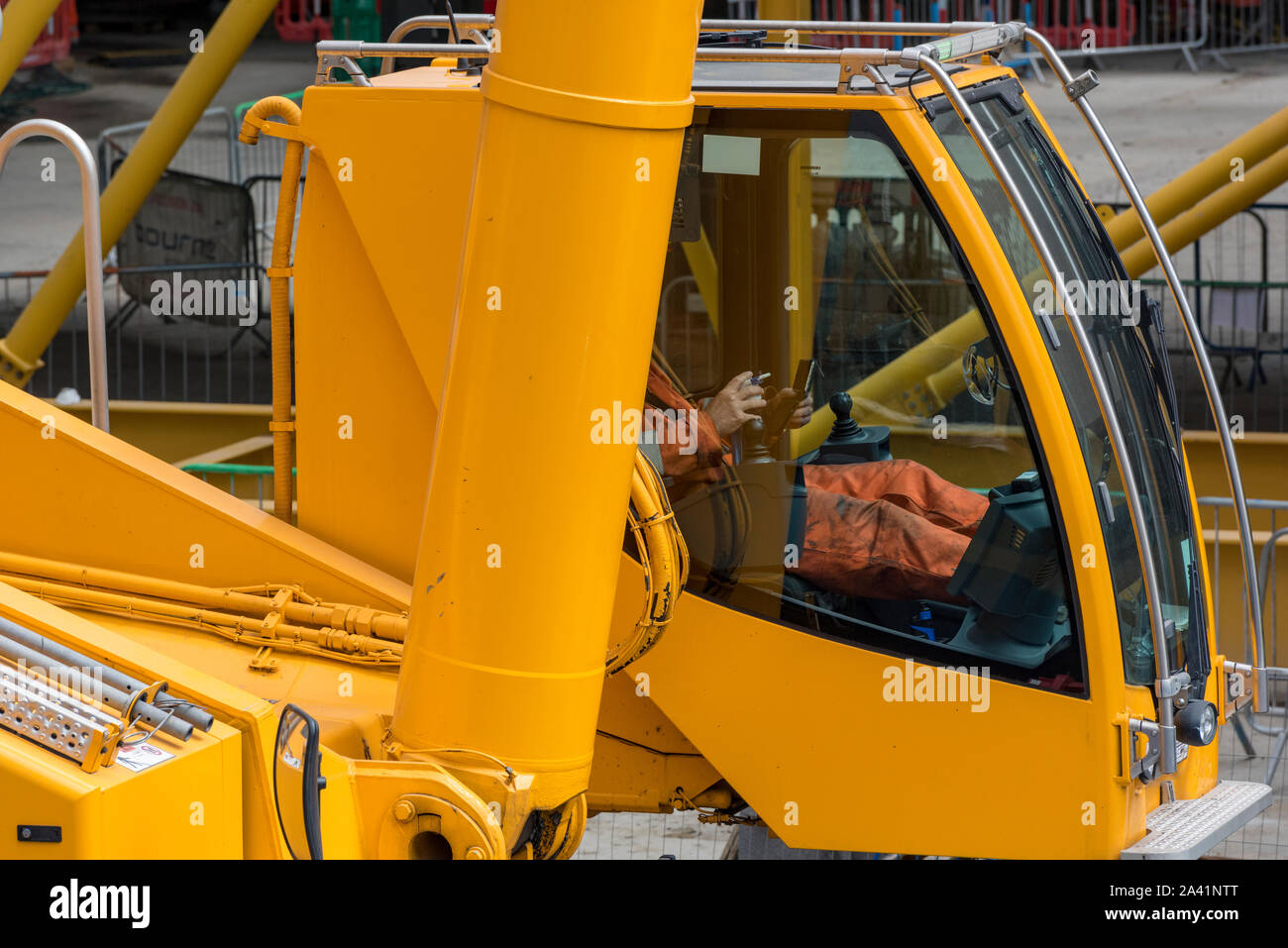 Building site machinery digger driver with feet up sitting in cab at controls of big earth mover digger. Stock Photo