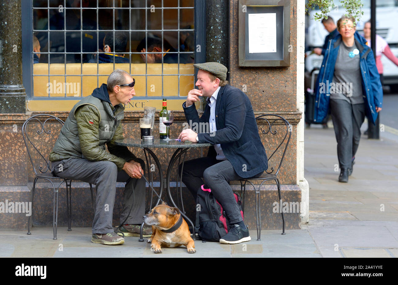 London, UK. Two men and a dog outside the Clarence pub in Whitehall. One drinking beer, the other wine Stock Photo