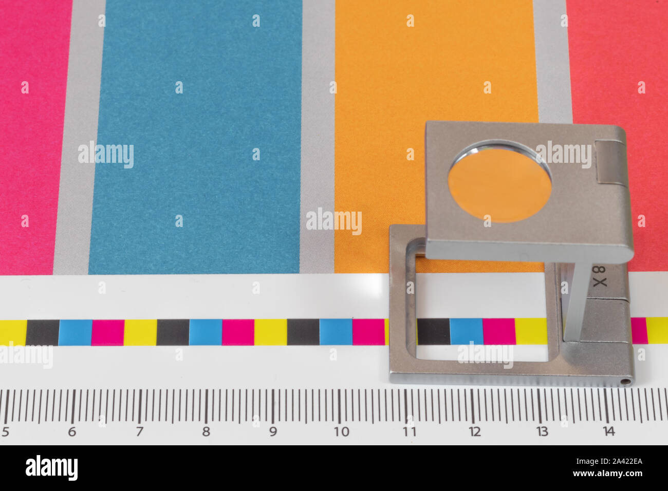 Silver magnifying glass standing on the test print, colored background. Print loupe on offset printed sheet with basic colors control bars. Stock Photo