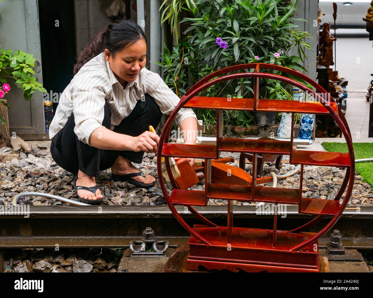 Asian woman varnishes woodwork on rail track in Railway village or Train Street, Hanoi, Vietnam, Asia Stock Photo