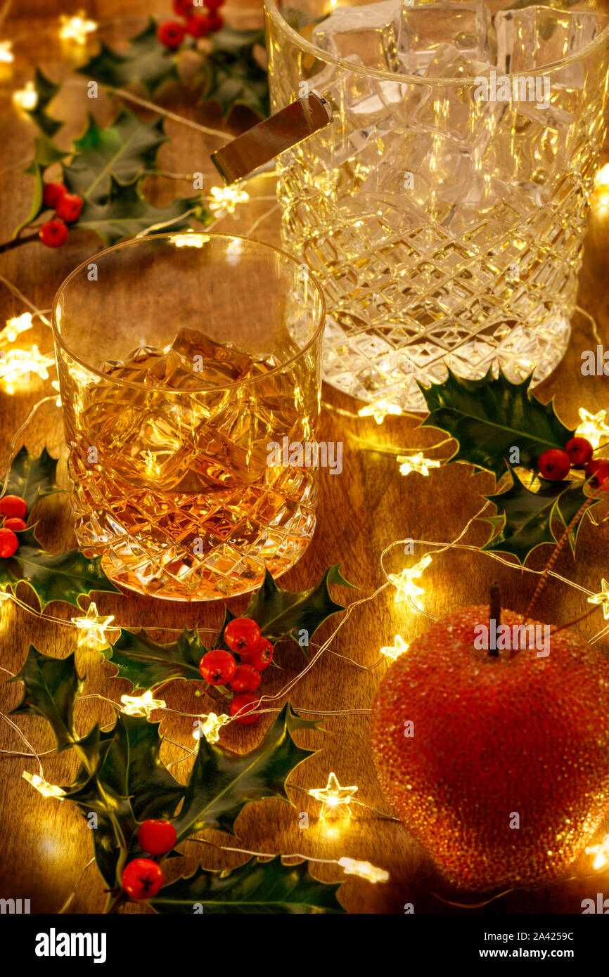 Crystal whisky ice bucket and a glass of whisky with christmas lights and holly berries, on a wooden table Stock Photo