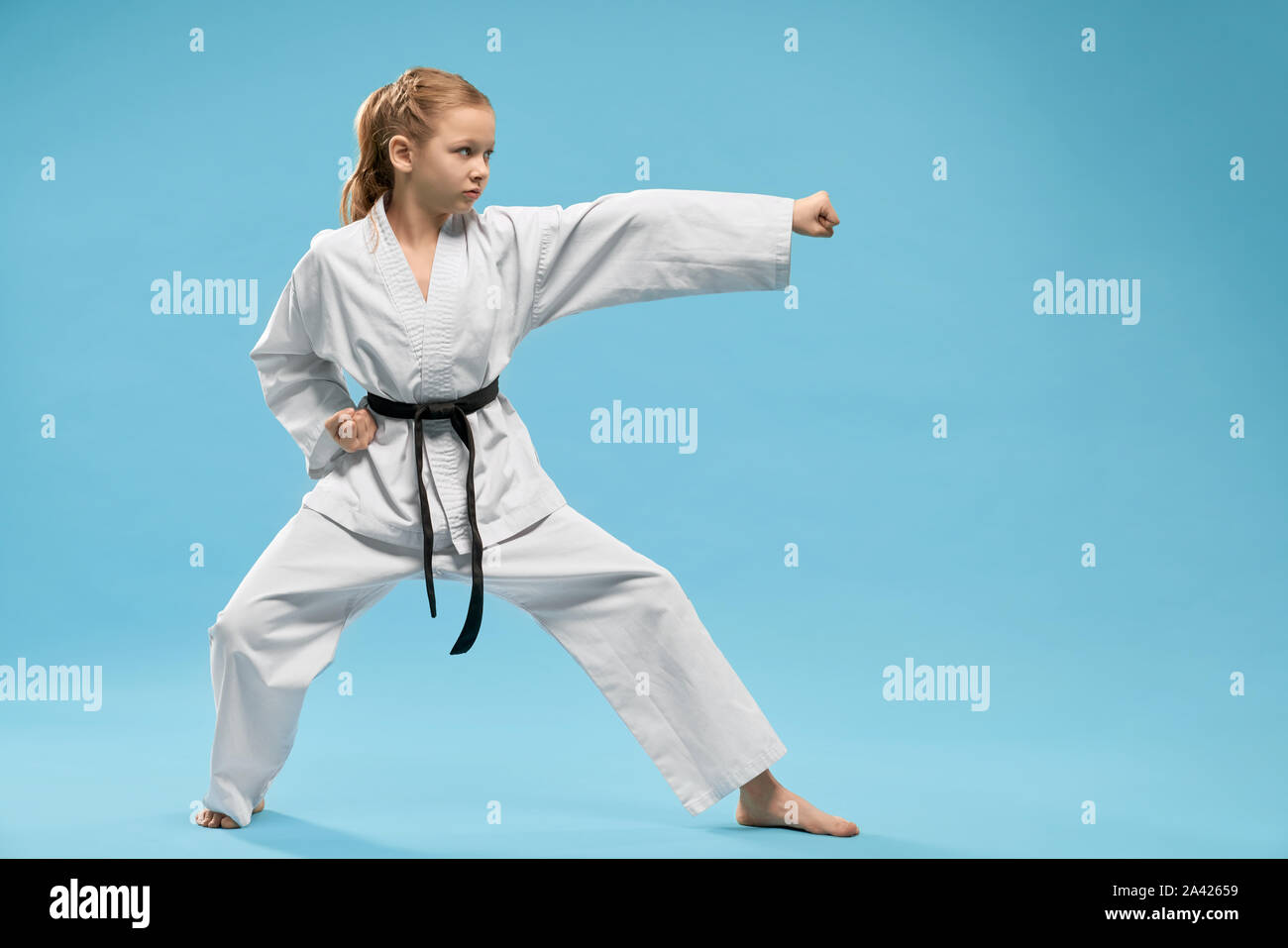 Pretty, young girl practicing karate and jujitsu. Confident junior wearing in white kimono with black belt standing in stance. Concept of wellness and martial arts. Stock Photo